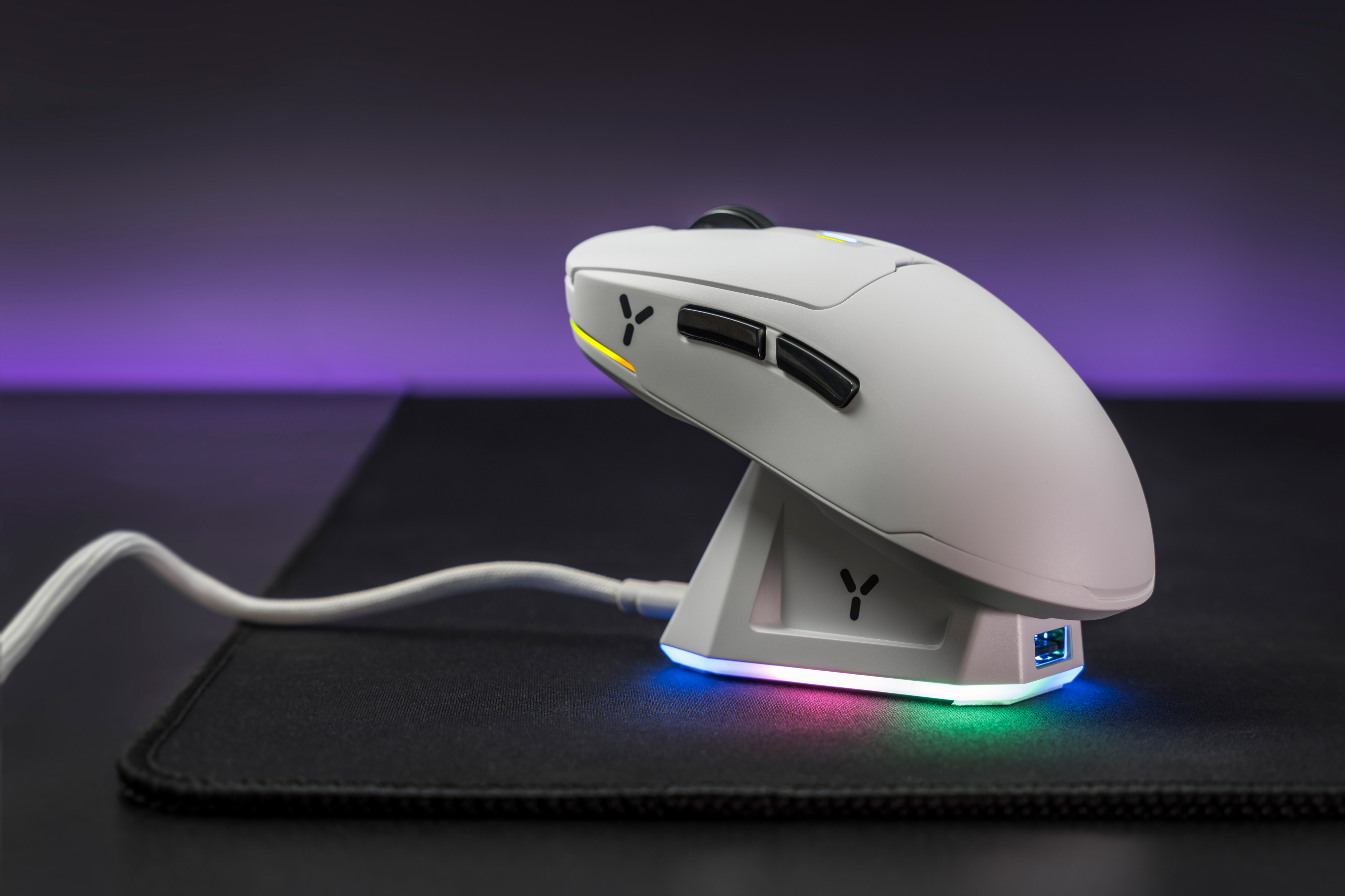 Biała bezprzewodowa mysz do gier z podstawką ładującą na czarnej podkładce pod mysz.