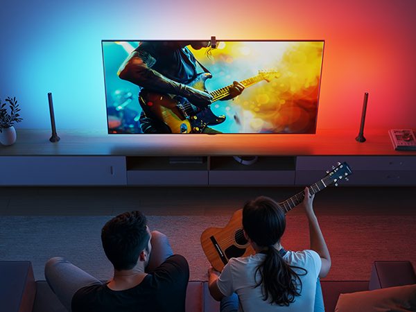 Zwei Personen sitzen auf dem Boden und sehen einen Mann Gitarre spielen.