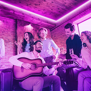 Eine Gruppe von Leuten versammelt, einer spielt Gitarre, mit lila Lichtern.