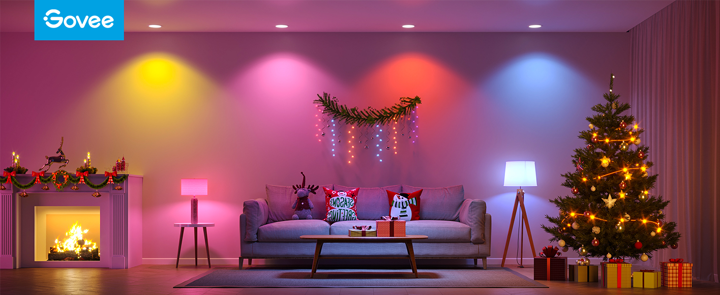 Ein Wohnzimmer mit intelligenten Lichtern, einem Weihnachtsbaum und einem Sofa. Verschiedene Farben an der Wand.