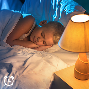 Ein Kind schläft im Bett, mit einer Lampe auf einem Nachttisch daneben.