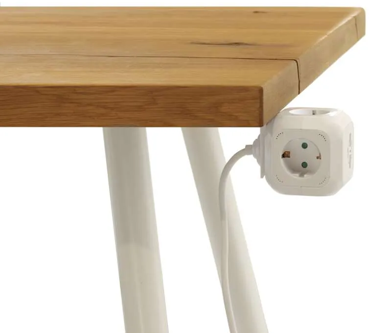 Egy fehér power cube egy fa asztalba dugva, a kocka a szélén lóg.
