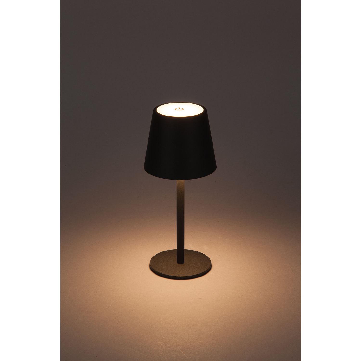 Een zwarte lampenkap op een dunne, lange, zwarte standaard. Het licht is aan.