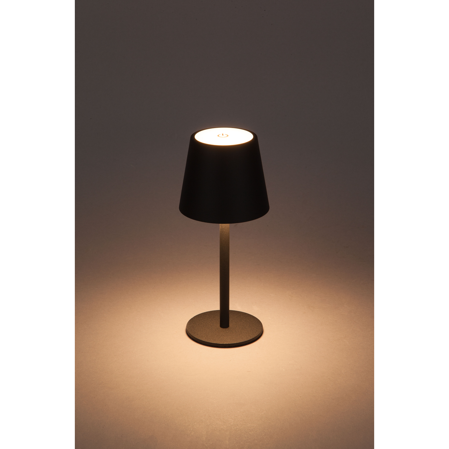 Zwarte lamp met een lampenkap, een dunne steel en een ronde basis. Het licht is aan.