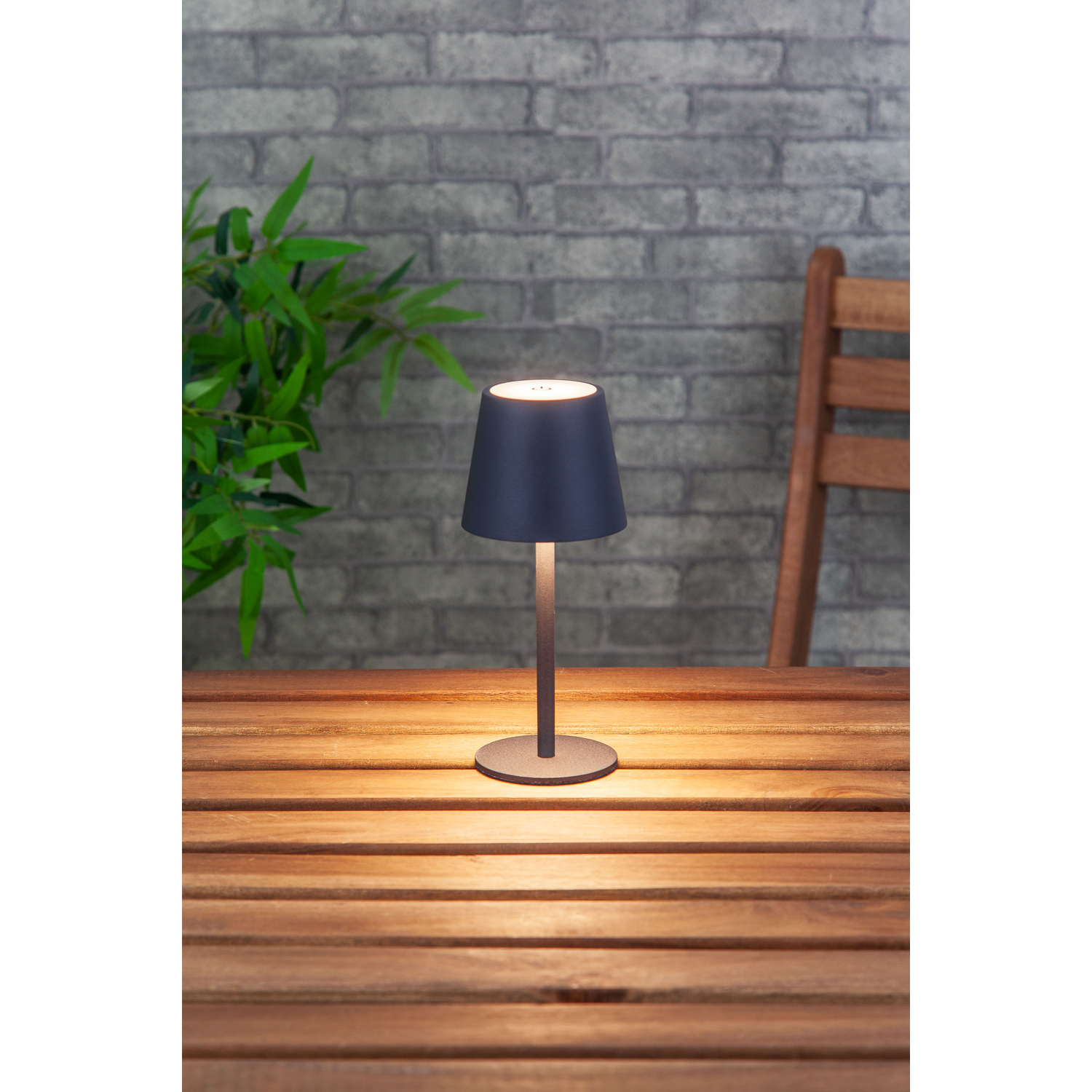Buiten tafellamp op een houten tafel met bakstenen muur en groen op de achtergrond.