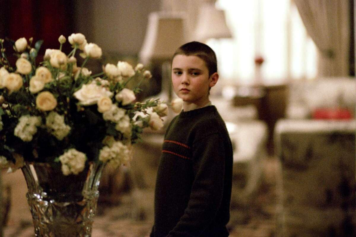Garçon aux cheveux courts près d'un vase de fleurs blanches et jaunes.