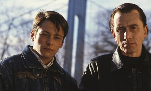 Une image fixe d'un film avec deux hommes, devant un arrière-plan flou d'un pont.