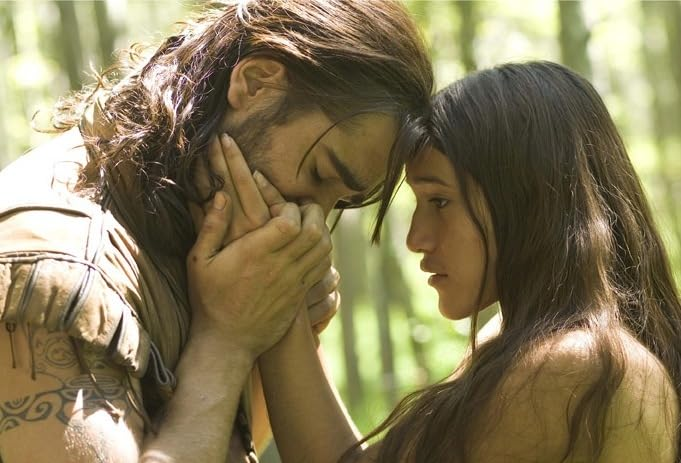 Un homme et une femme se font face, se touchant le visage, dans un cadre forestier.