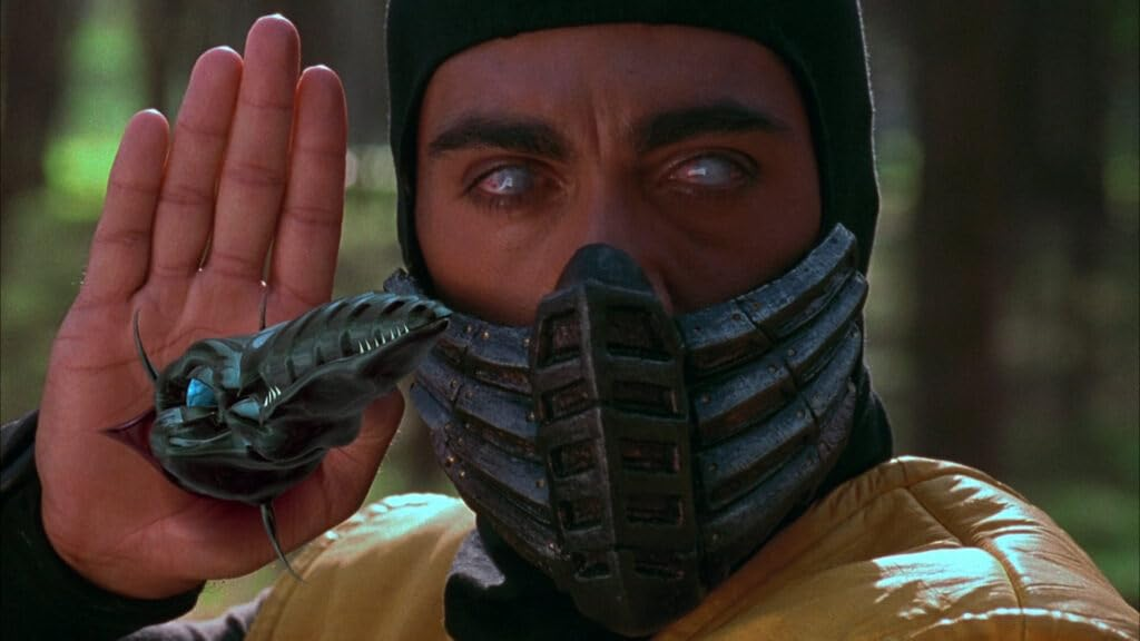 Een man met een zwart masker met een slangachtig object in zijn hand, uit een film.