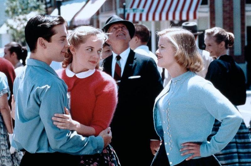 Een scène uit een film met drie mensen in retrokleding op straat.