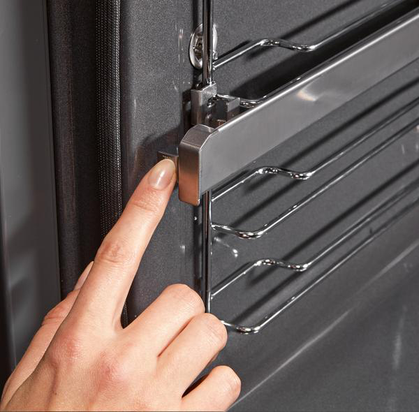 Eine Hand, die ein Metallgestell in einen Ofen legt. Der Ofen ist dunkelgrau mit silbernen Rosten.