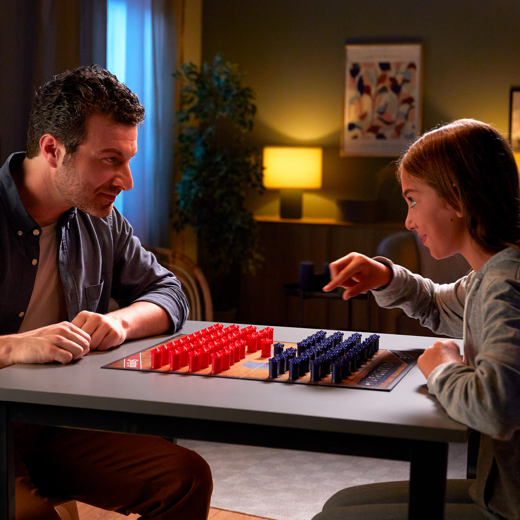 Vader en dochter spelen een bordspel. Rode en blauwe pionnen op een bord.