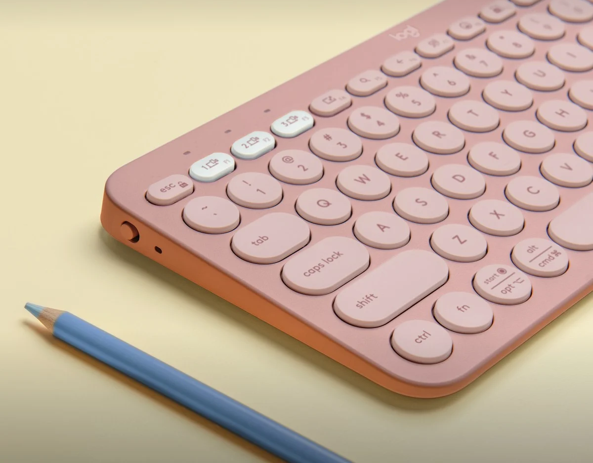Egy rózsaszín Logitech billentyűzet világossárga háttérrel és egy kék ceruzával.