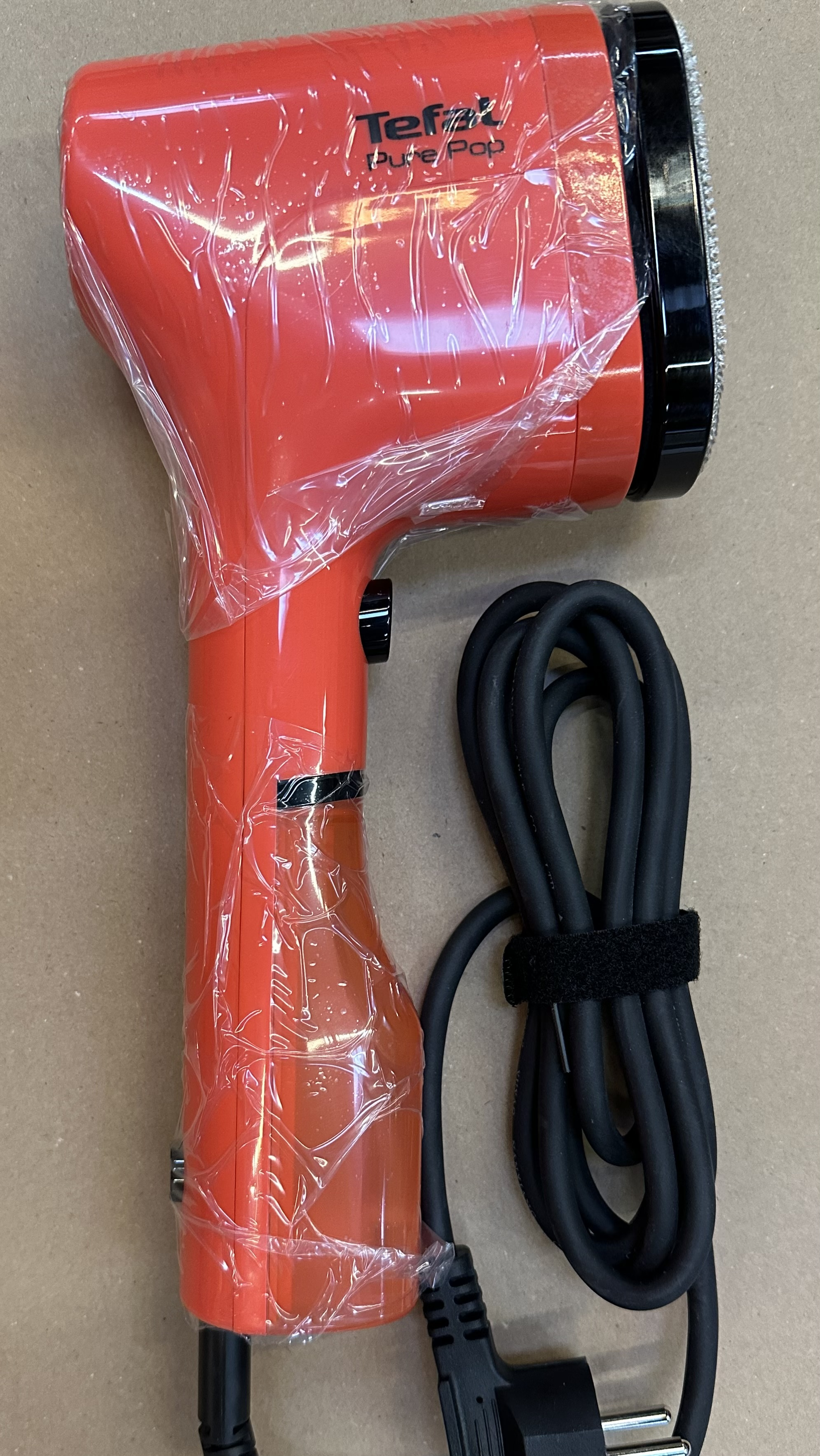Pomarańczowa parownica do ubrań Tefal Pure Pop, zapakowana w plastik.