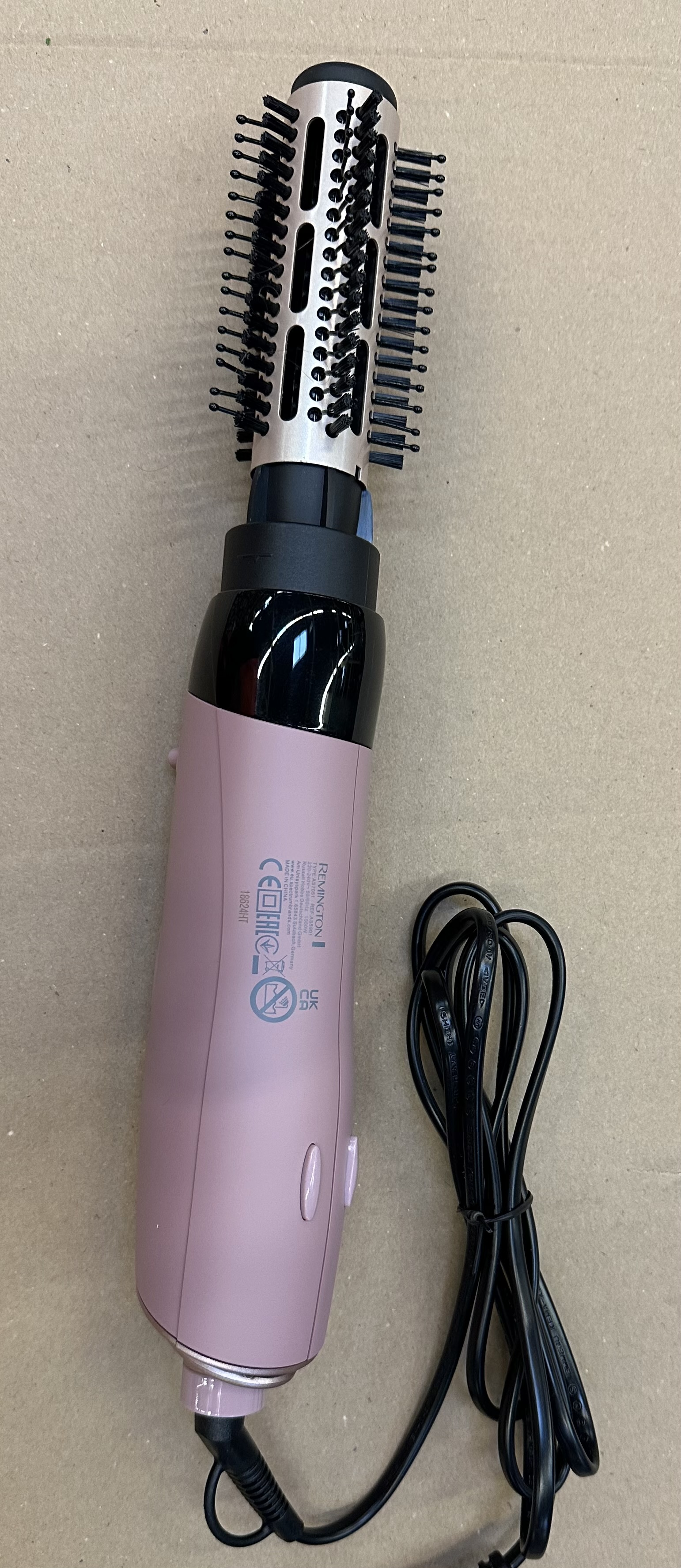 Różowa lokówka z szczotką i czarnym przewodem zasilającym.