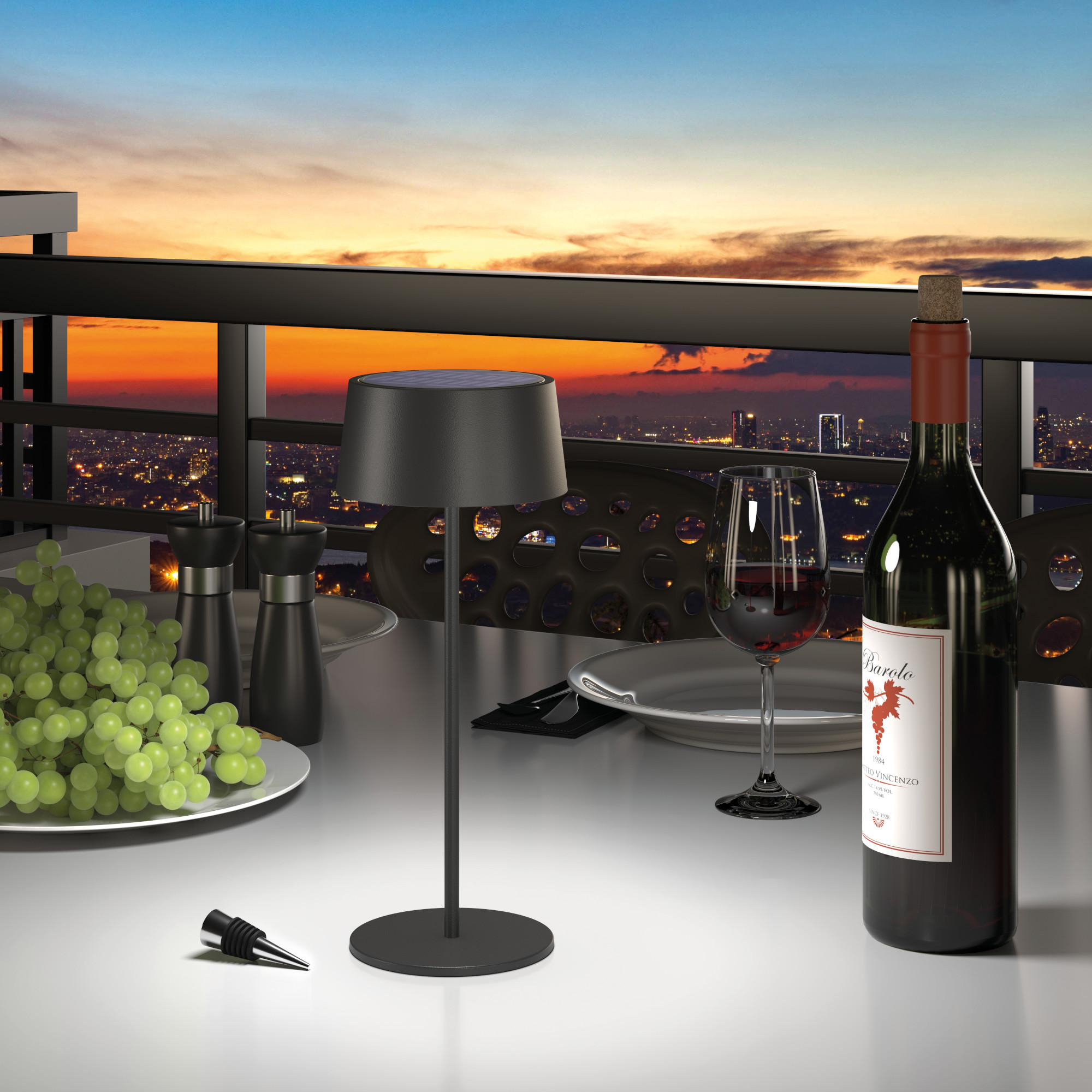 Tischszene im Freien mit Lampe, Weinflasche, Glas, Trauben und Skyline, Sonnenuntergang.