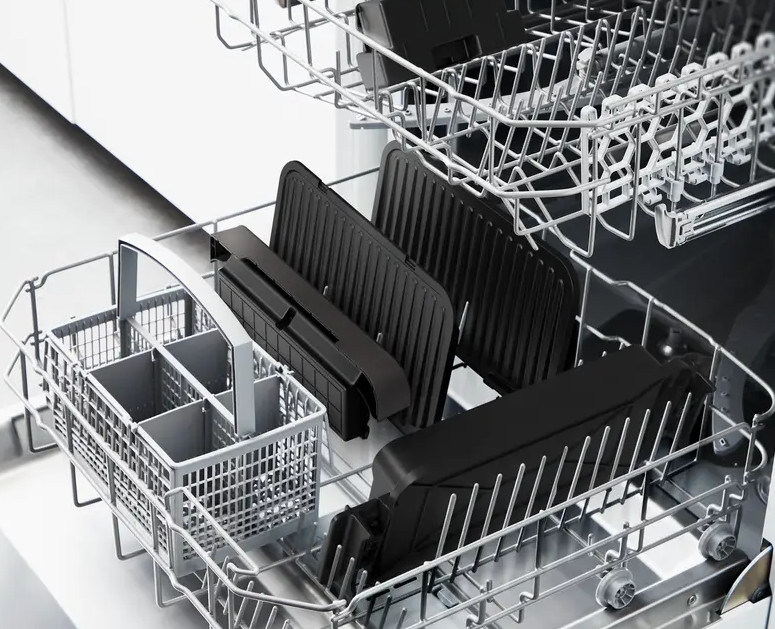 Wnętrze zmywarki wypełnione czarnymi przedmiotami nadającymi się do mycia w zmywarce.
