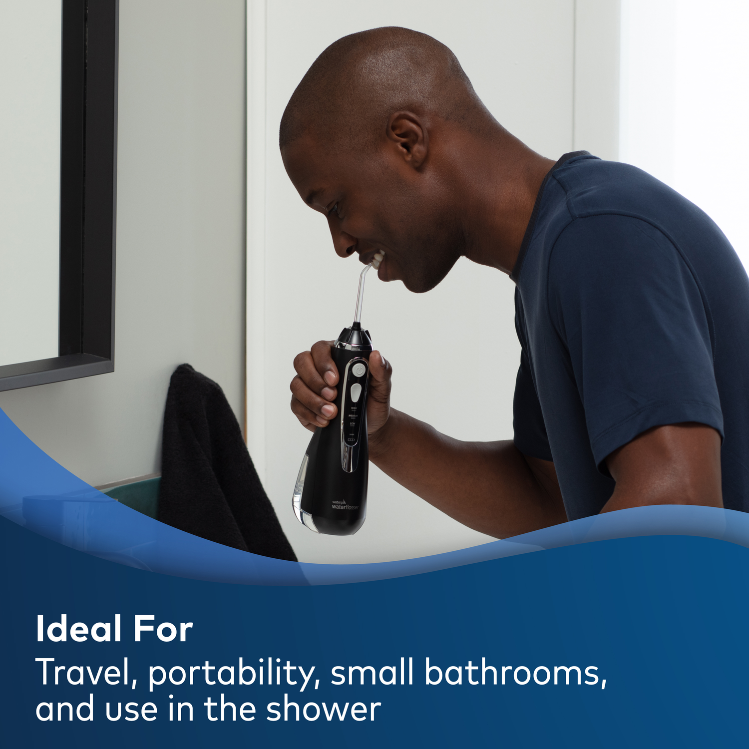 Man using a black Waterpik water flosser in a bathroom. Text reads 'Ideal For Travel, portability, small bathrooms, and use in the shower'.