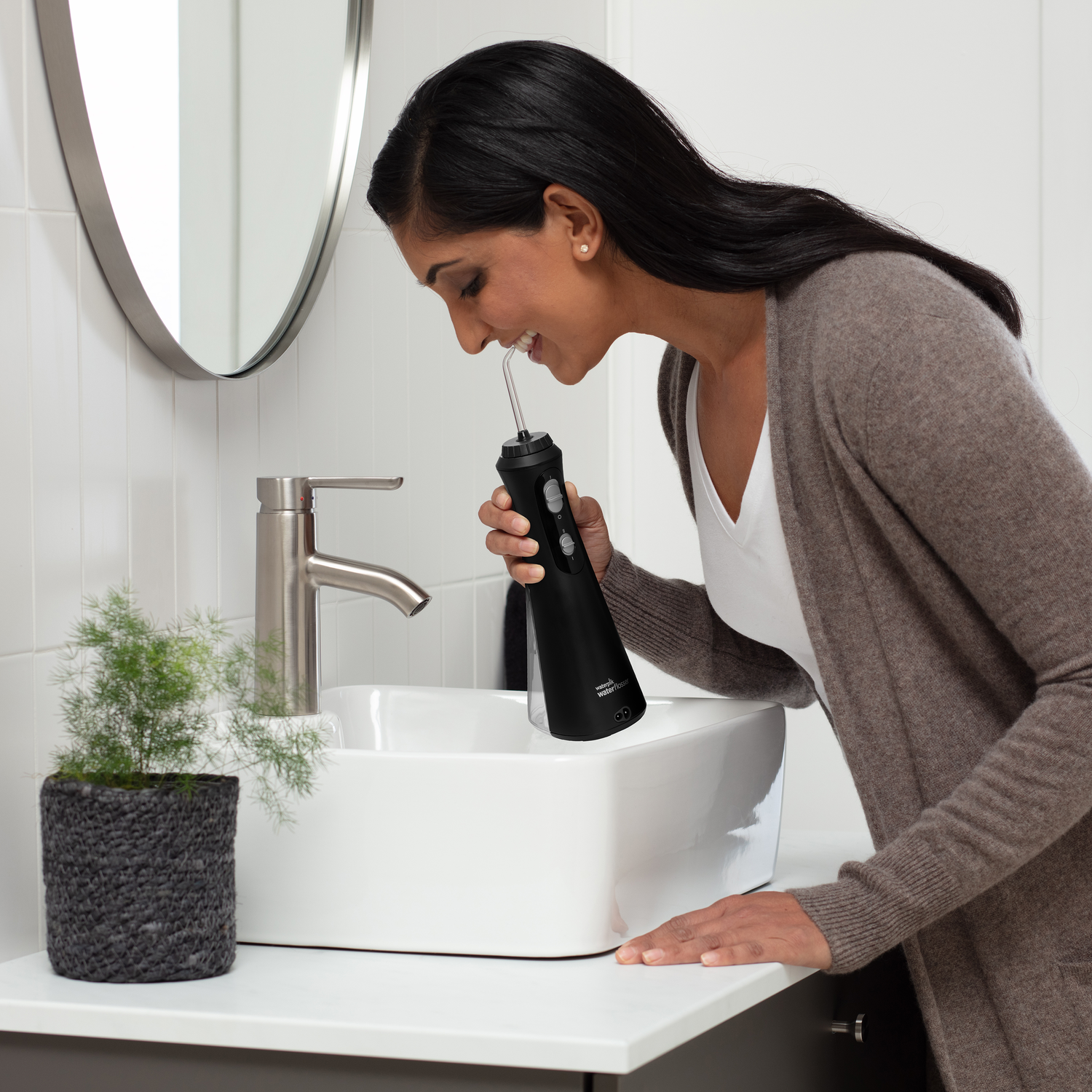 Woman using a black water flosser over a sink.
