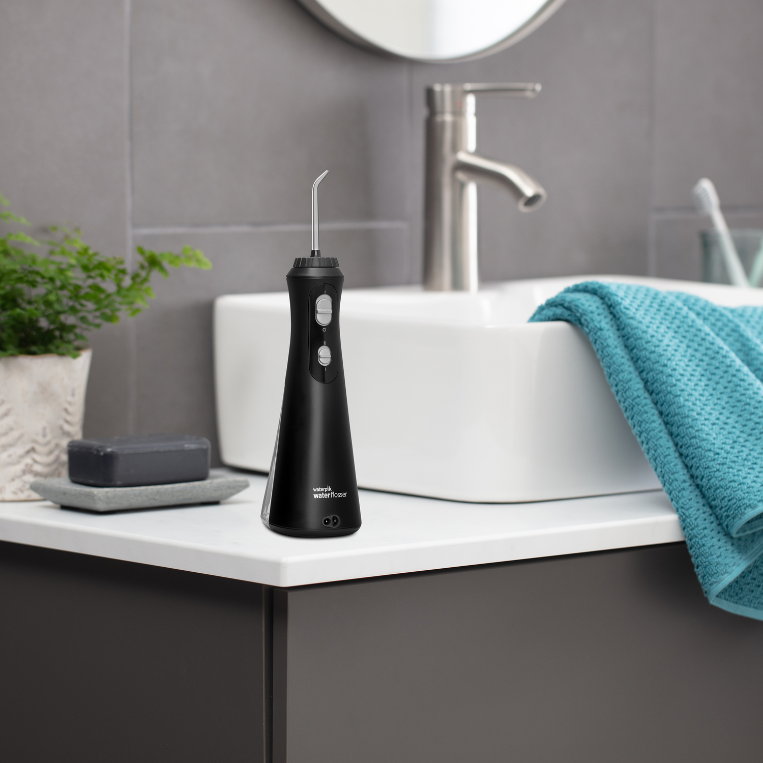 Black water flosser on a countertop. A sink, mirror, and a plant are in the background.