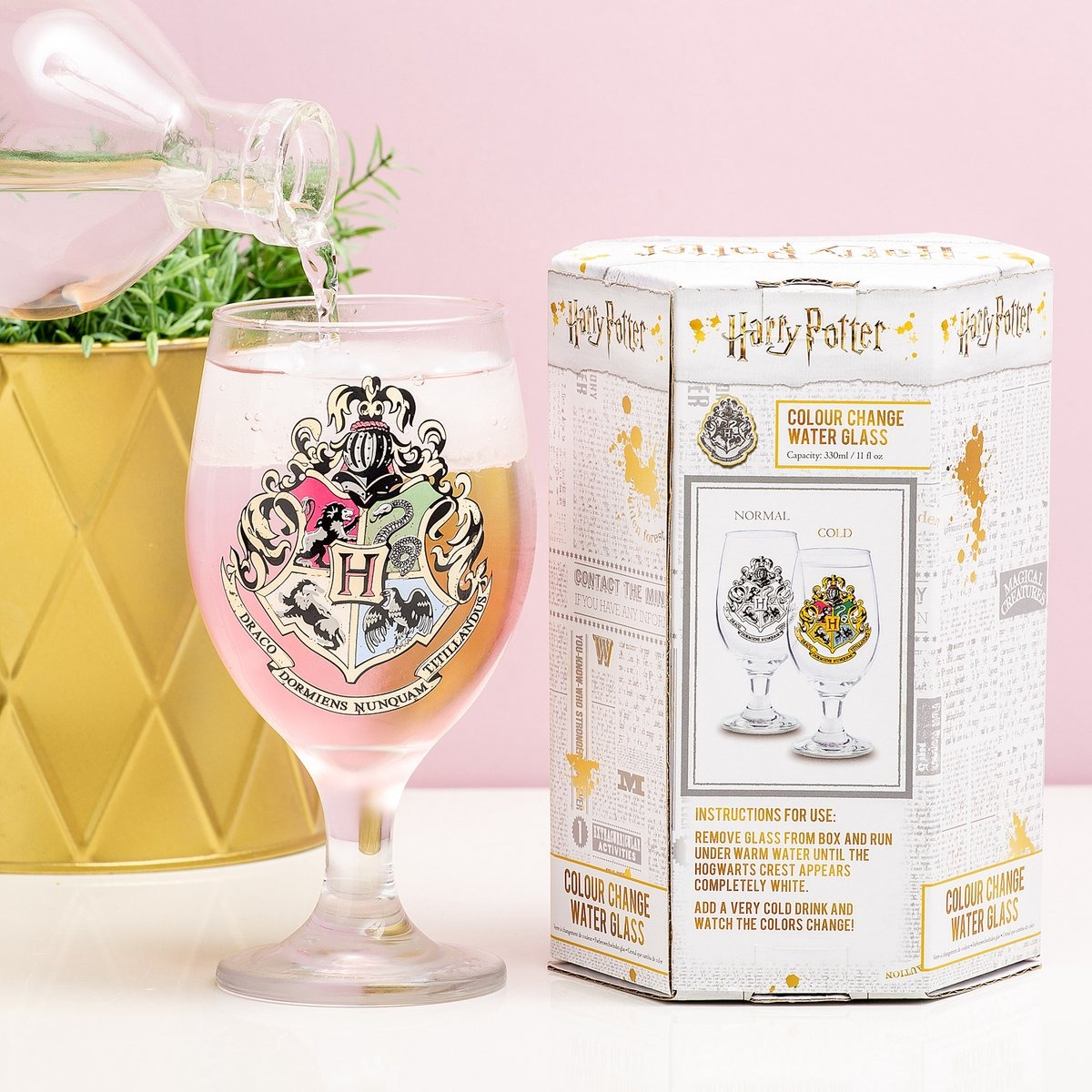 Glass with a Harry Potter crest, pink liquid being poured, and a color-changing box.