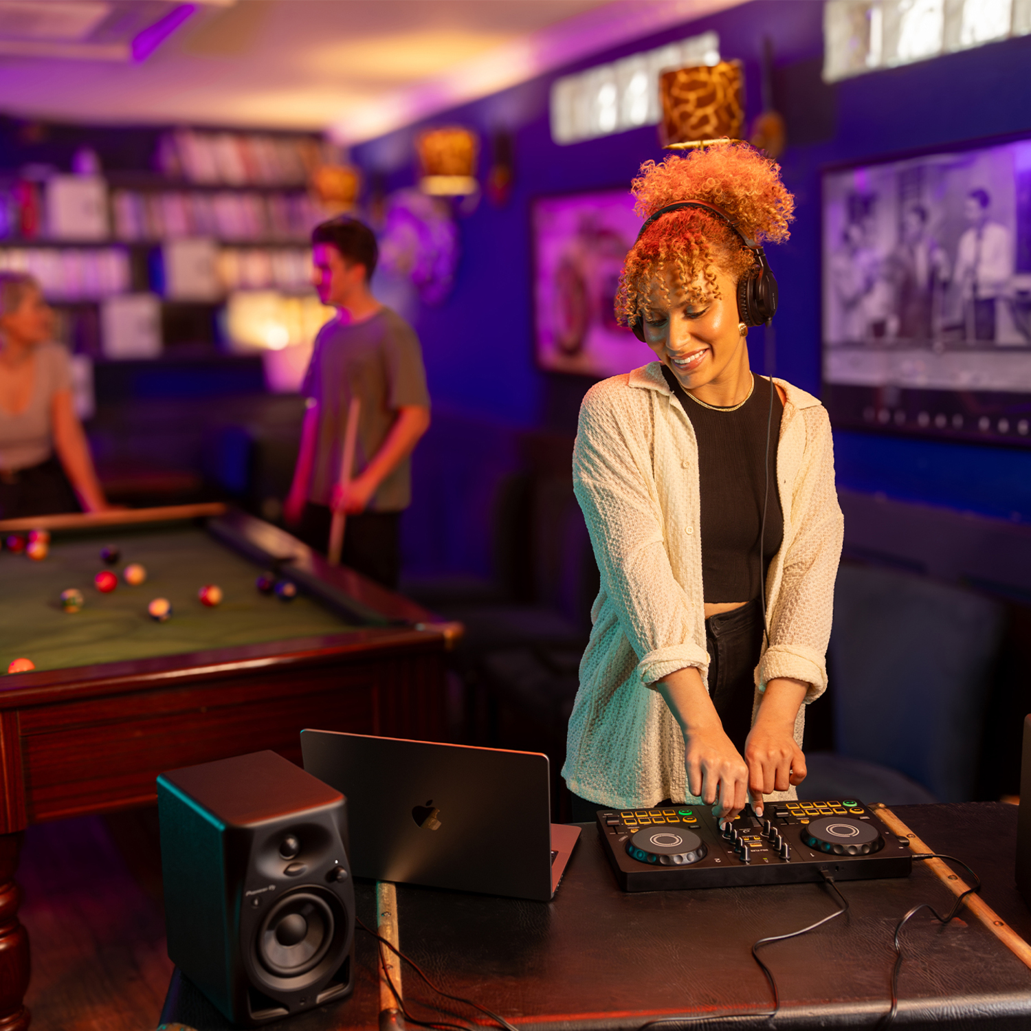 Vrouw aan het draaien met een koptelefoon en een mixer, met een laptop en een luidspreker, in een club.