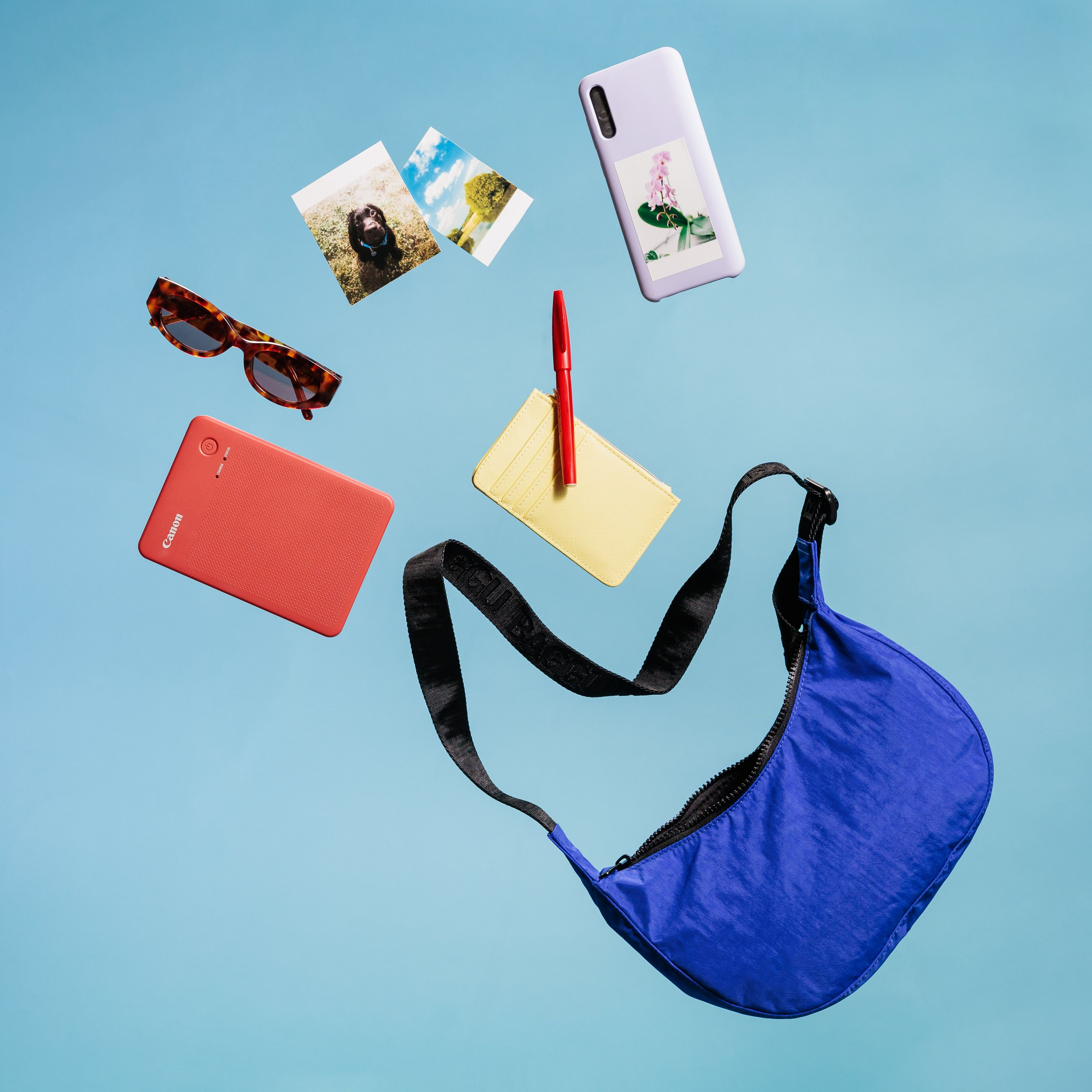 Oggetti fluttuanti in aria su sfondo blu: occhiali da sole, foto, telefono, borsa, penna e portafoglio.