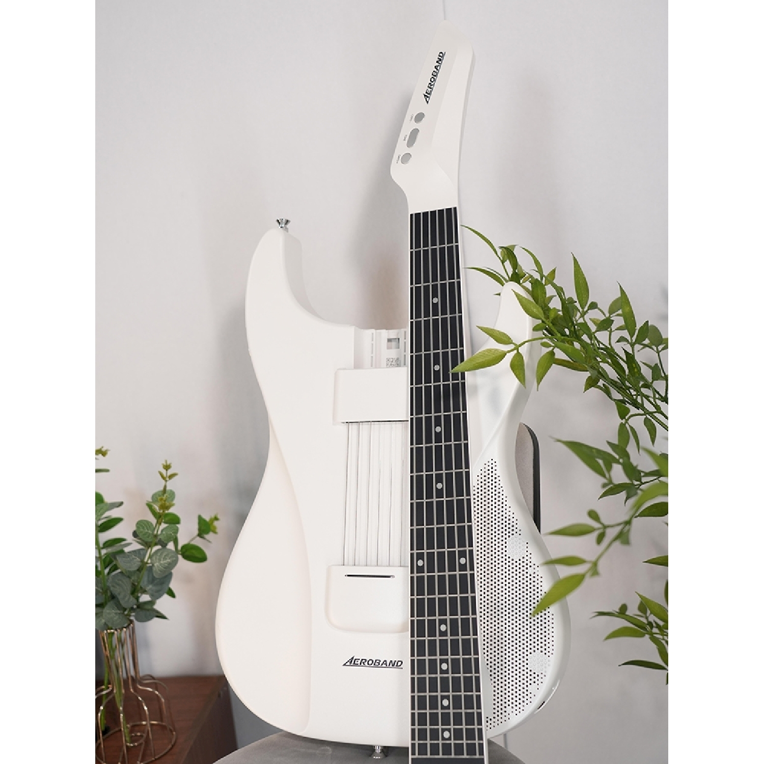 Chitarra elettrica bianca appoggiata a un muro bianco. Piante visibili sul lato.