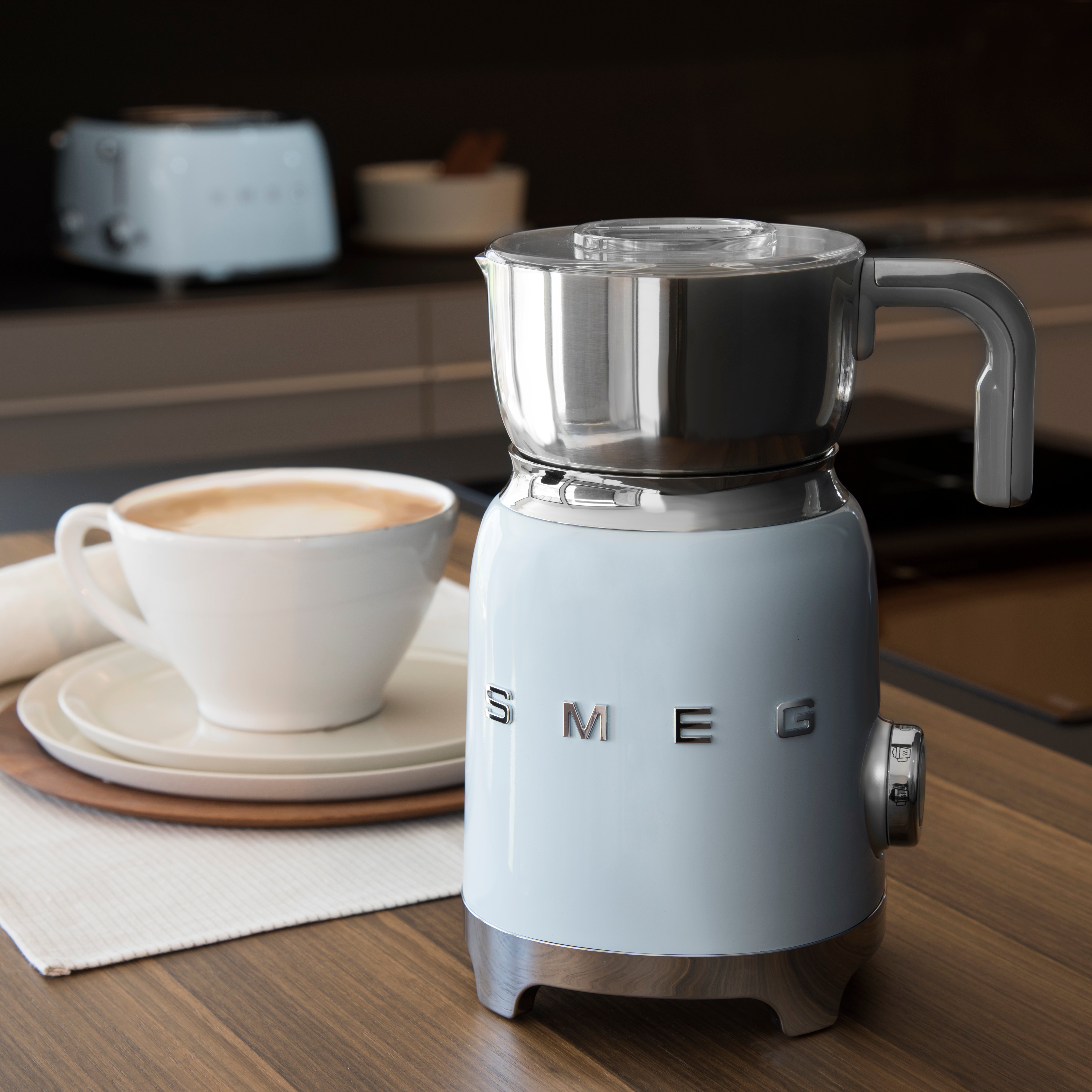 Un mousseur à lait SMEG bleu clair et une tasse blanche avec un latte sur un comptoir.