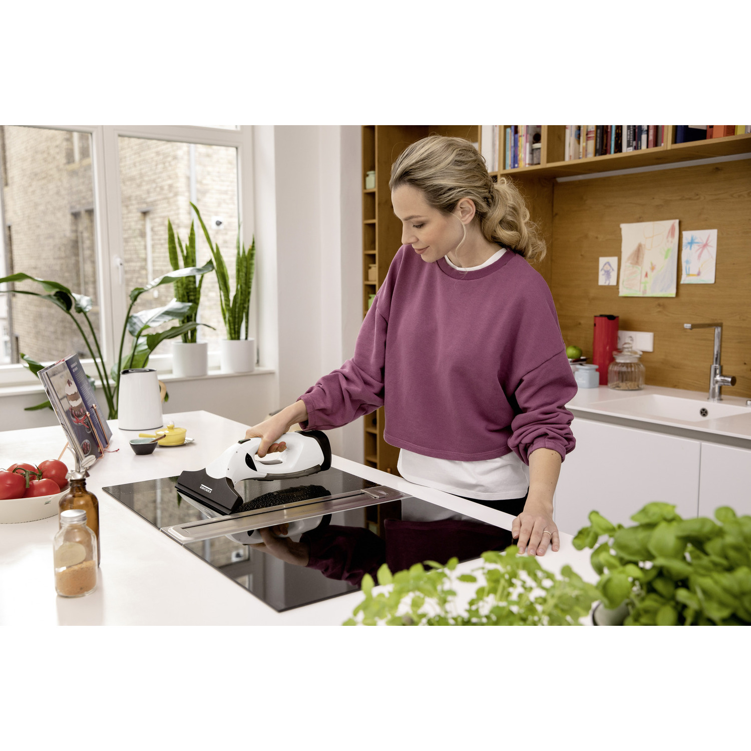 Woman cleaning a black stovetop with a white appliance. Kitchen setting with white and wood. 