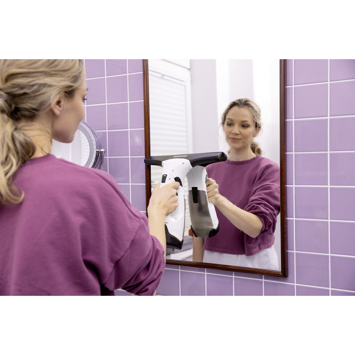 Woman cleaning a mirror with a white and black window cleaner in a bathroom.