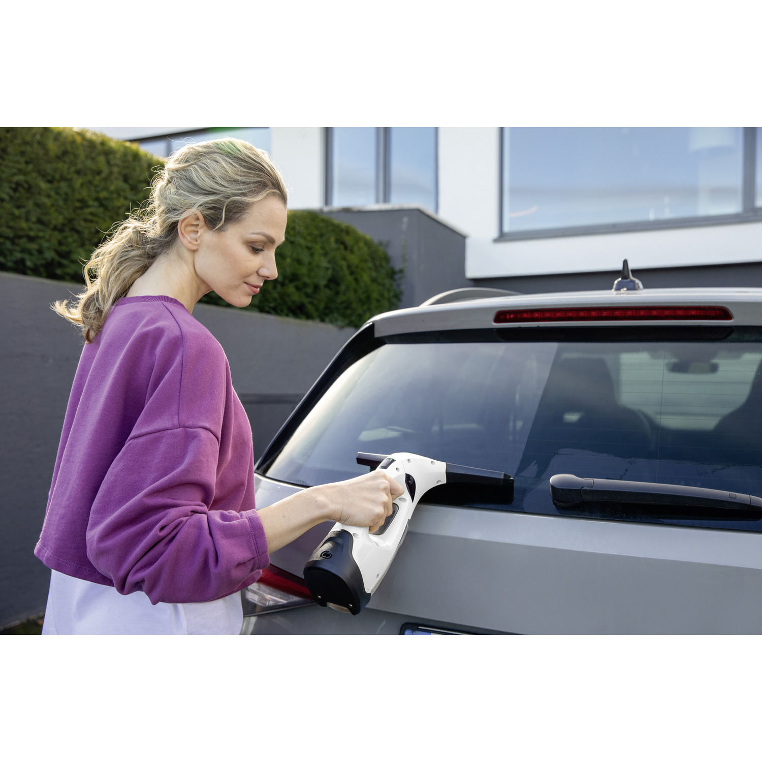 Woman cleaning a car window with a white and black window cleaner outdoors.