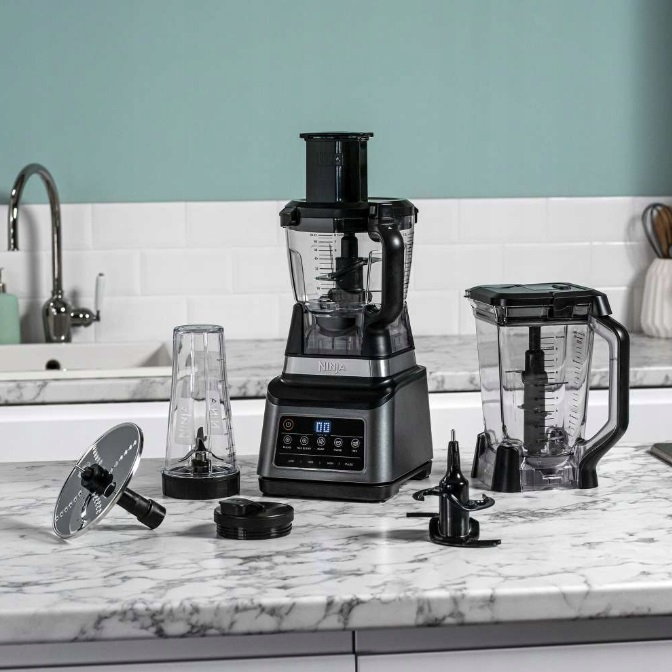 Zestaw urządzeń kuchennych Ninja z blenderem, robotem kuchennym i akcesoriami na marmurowym blacie.