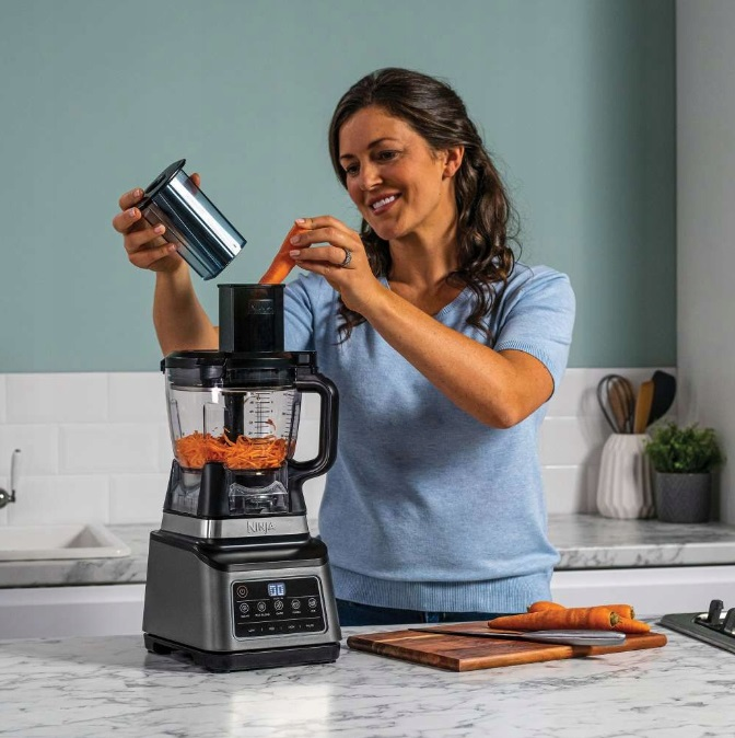 Kobieta dodaje marchewkę do robota kuchennego Ninja, tło kuchni.