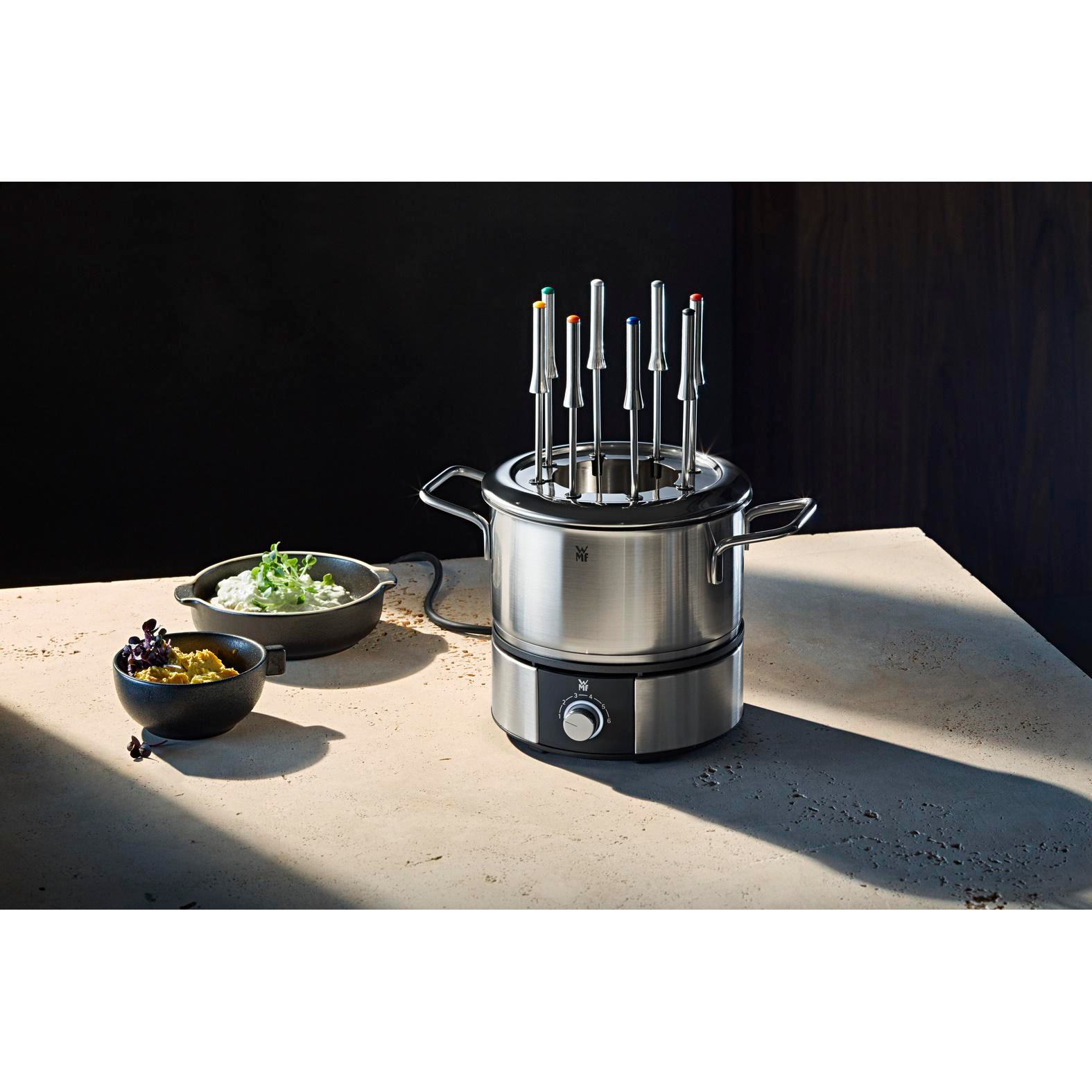 Fondue-Set auf einem Tisch mit Essen. Der Edelstahltopf hat eingelegte Spieße.