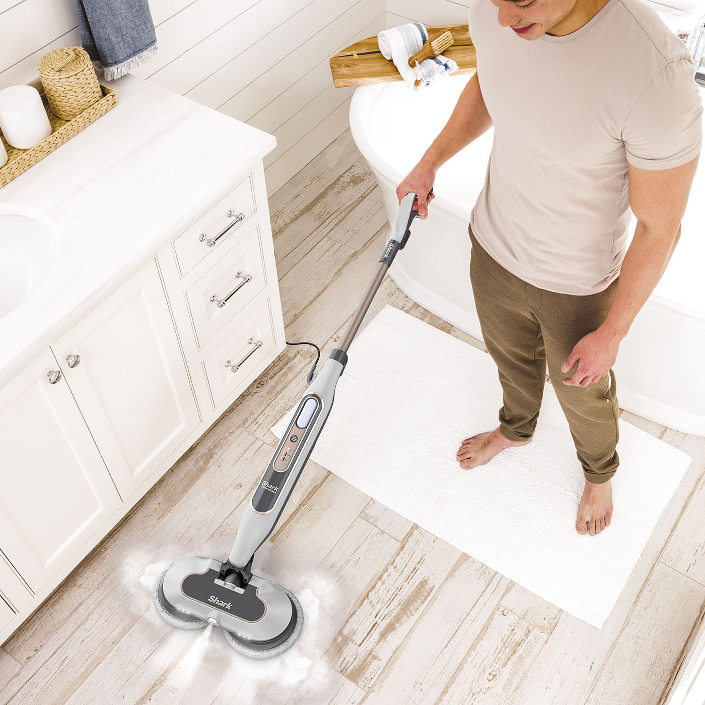Un homme nettoie le sol de la salle de bain avec une vadrouille à vapeur. Un tapis blanc est sur le sol.