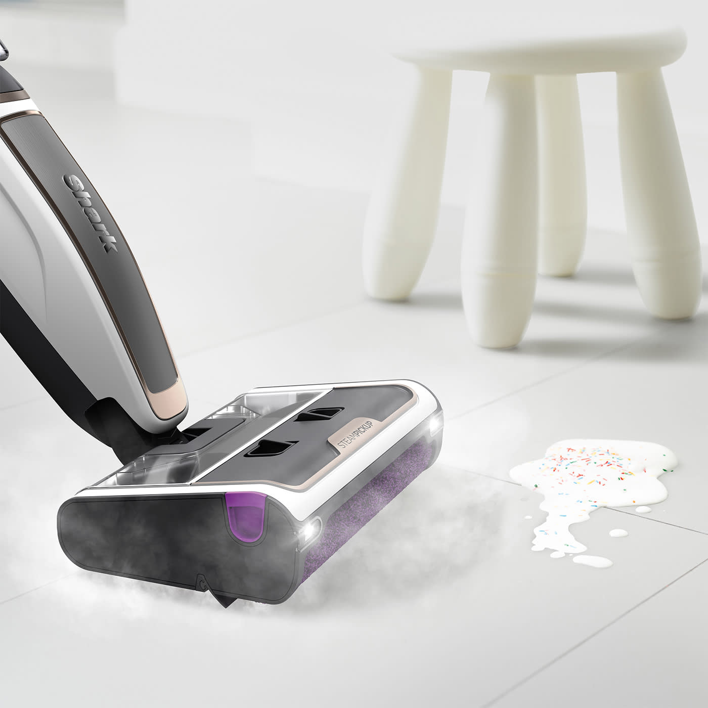 Nettoyeur vapeur nettoyant un sol carrelé blanc avec du liquide renversé et des vermicelles à proximité.