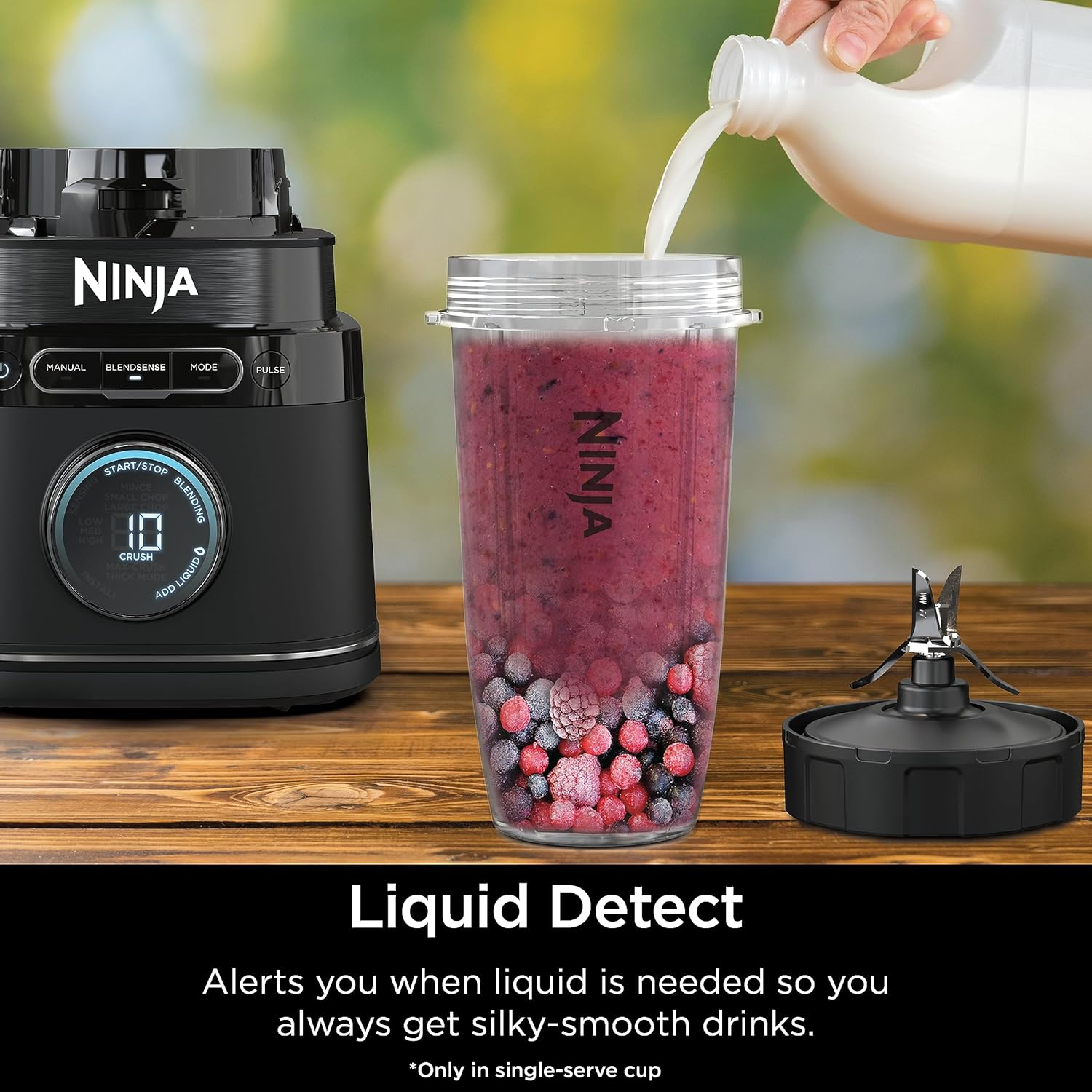 Ein Mixer mit einem Smoothie, der zubereitet wird. Eine Hand gießt Flüssigkeit hinein.