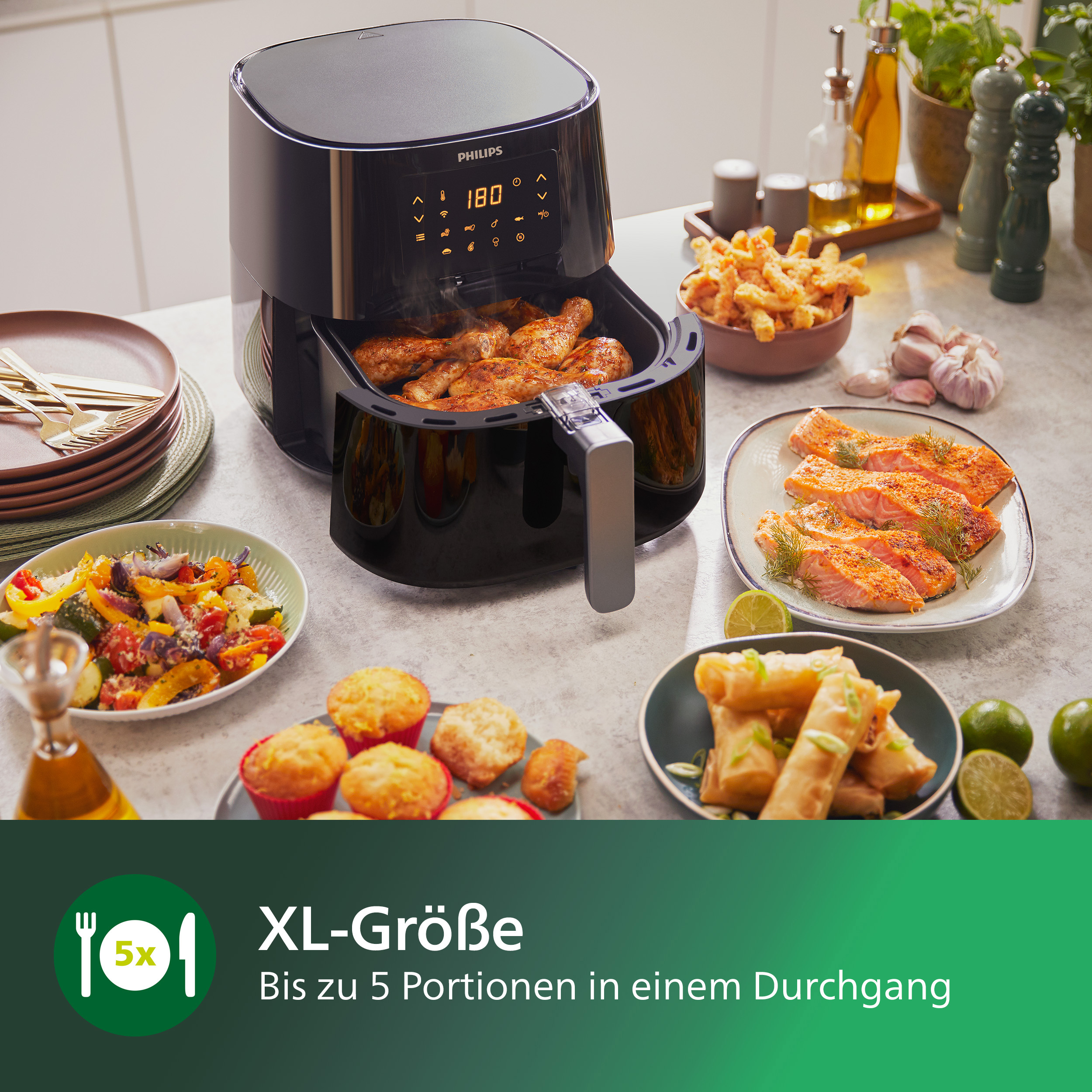 Heißluftfritteuse mit gekochtem Hähnchen und verschiedenen Beilagen auf einem Tisch.