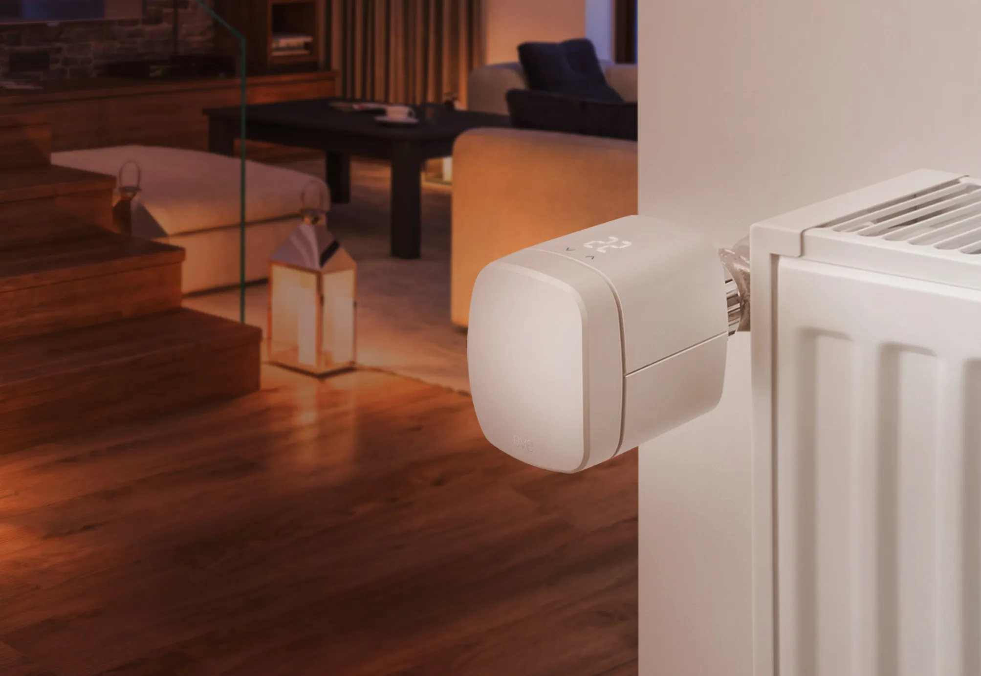 Thermostat au mur à côté d'un radiateur, avec un salon en arrière-plan.