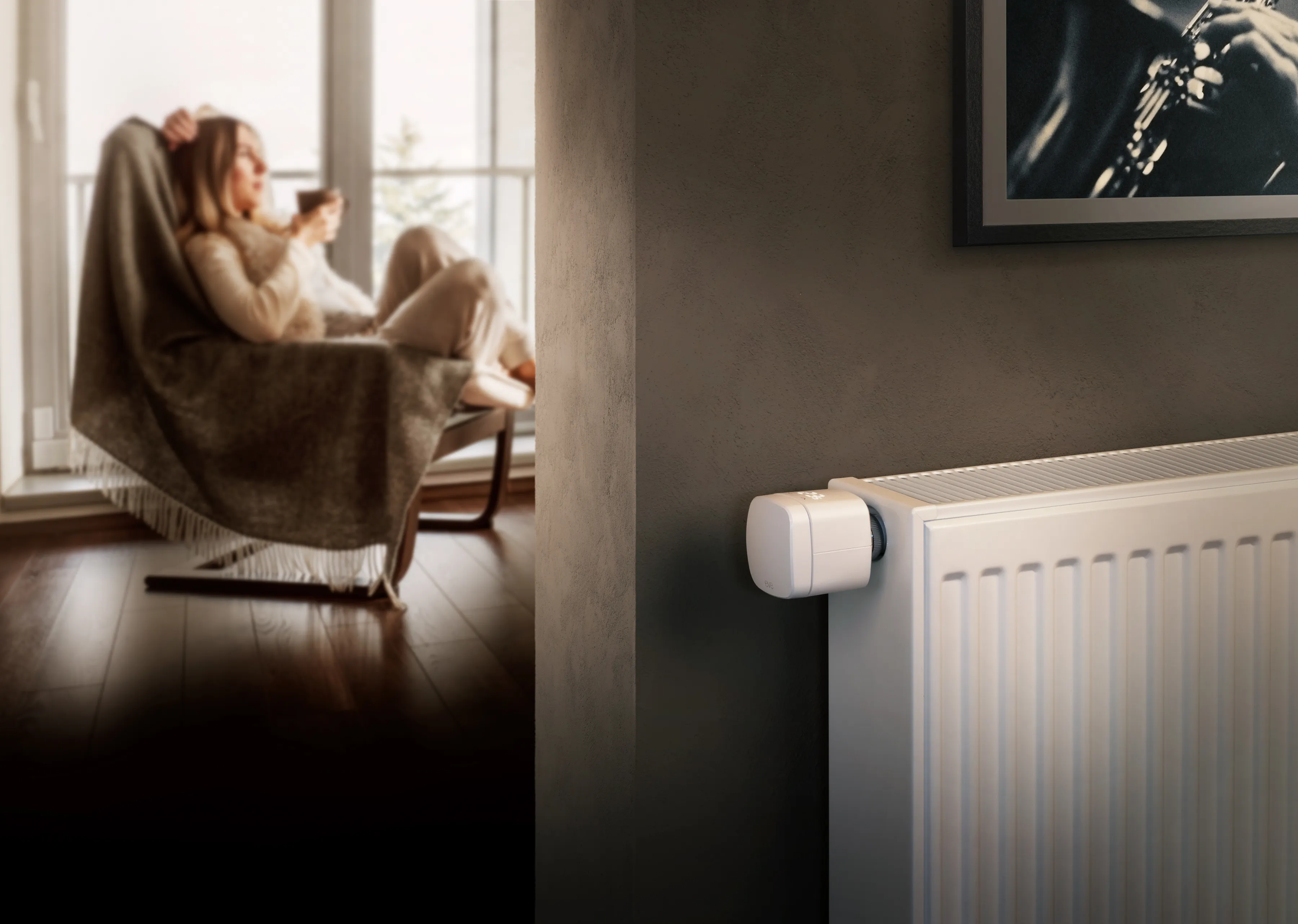 Thermostat intelligent sur un radiateur dans une pièce avec deux personnes à l'arrière-plan.
