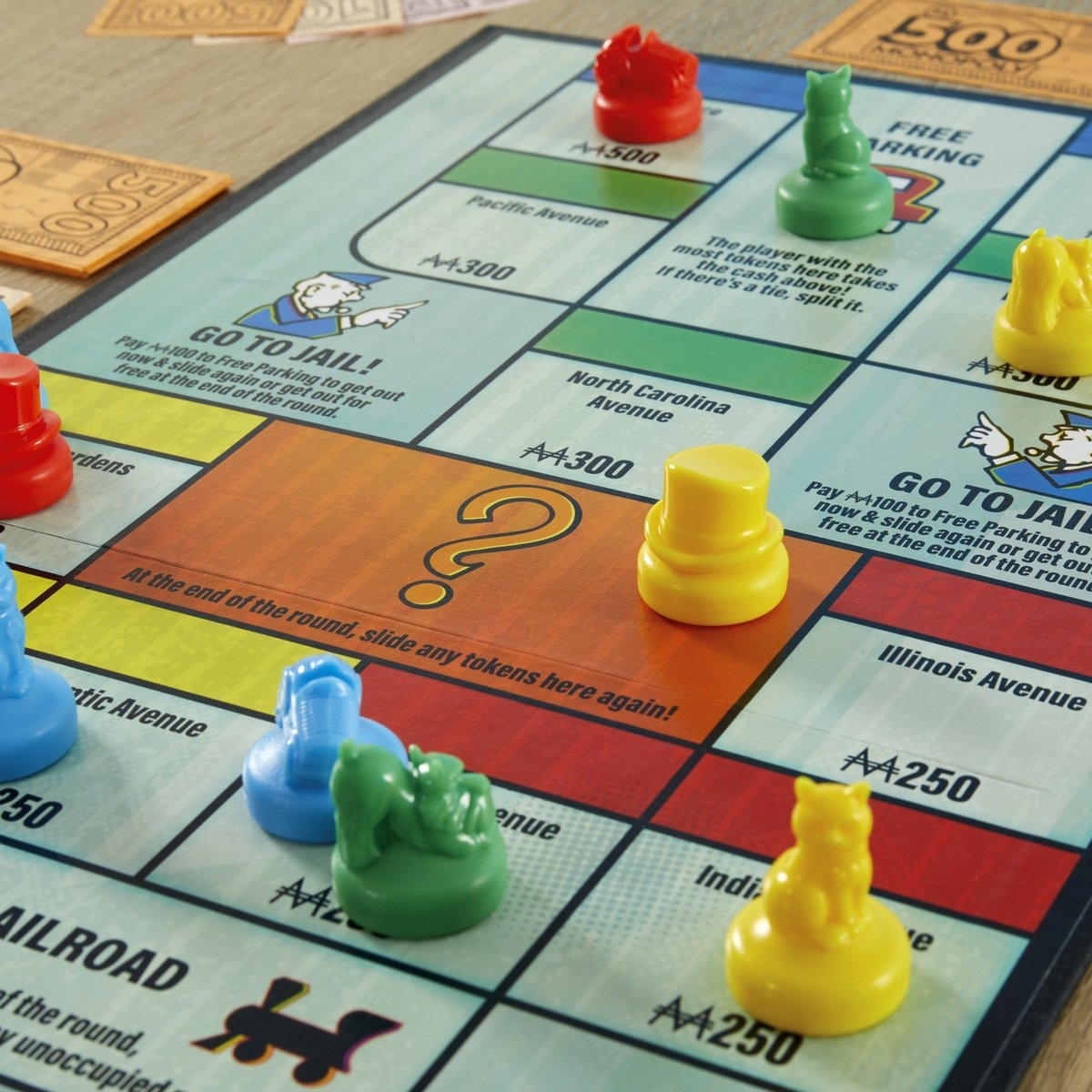 Monopoly board game. Red, green, yellow, and blue tokens on the board. Monopoly money scattered around.