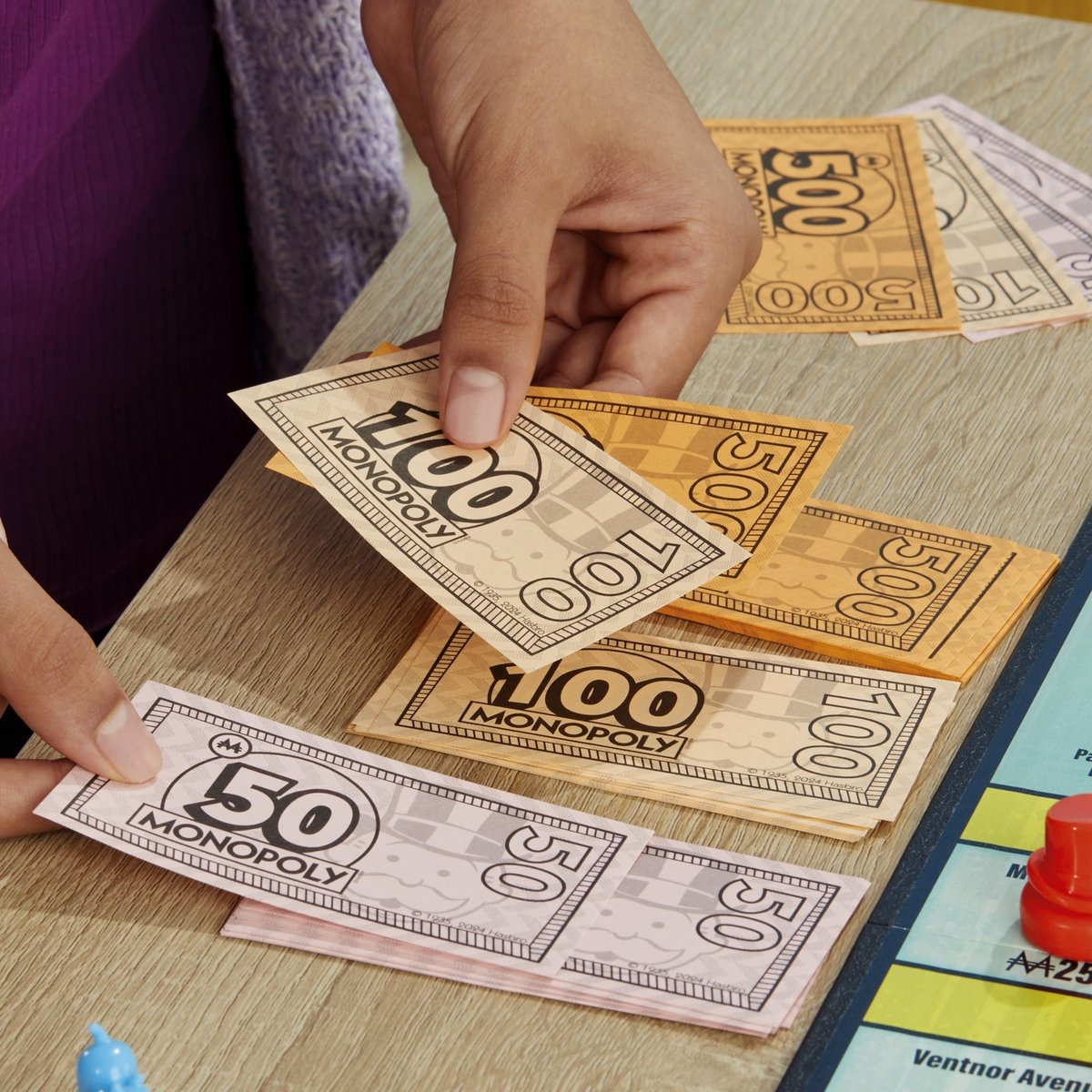 Person's hand holding Monopoly money. Other Monopoly money and game pieces are visible on table.