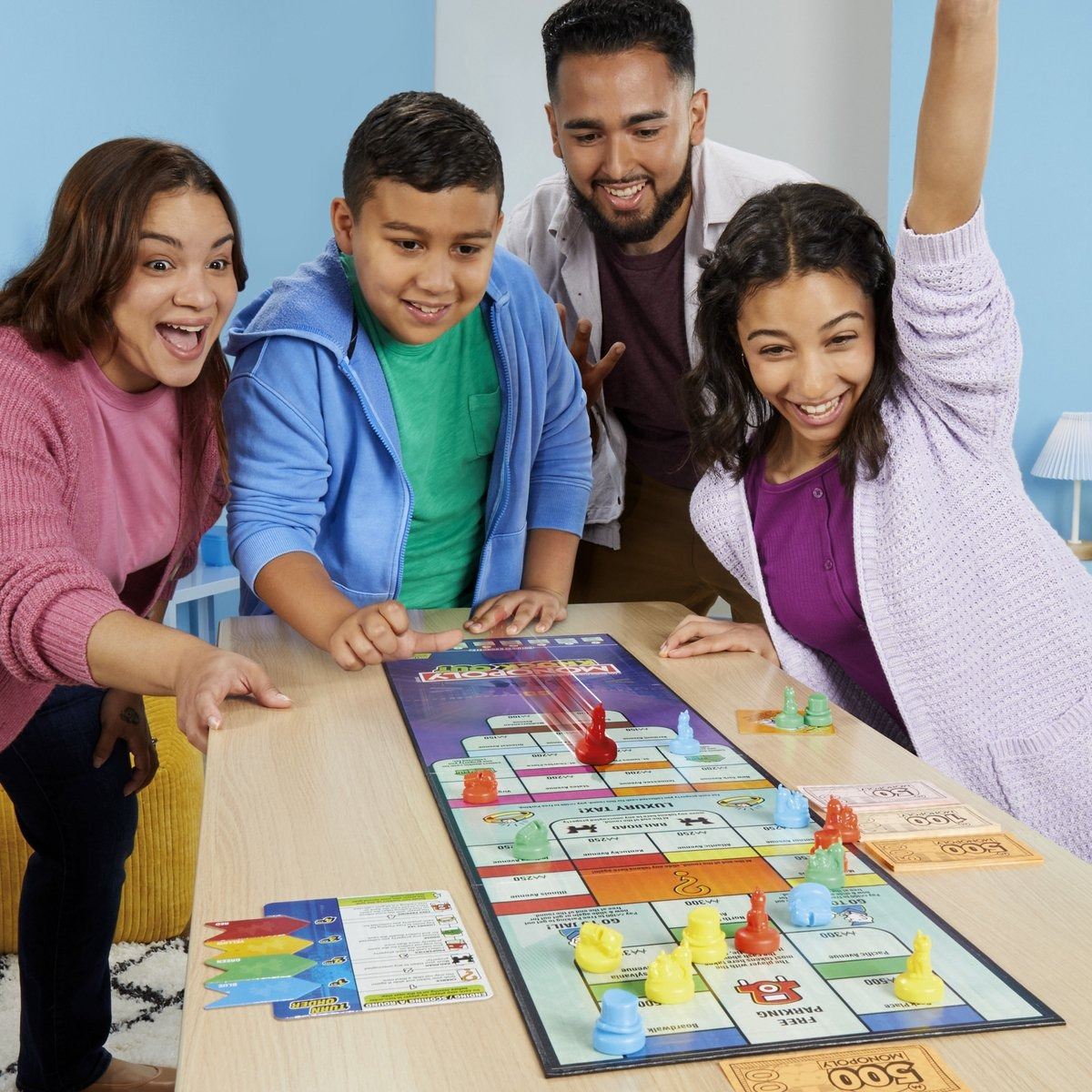 Four people playing Monopoly. The board game is on a table. They are smiling and excited.