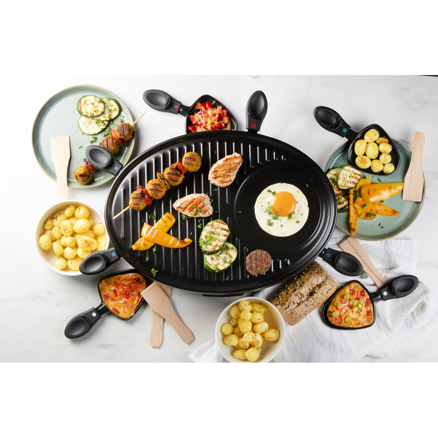 A raclette grill with food like potatoes, vegetables, and meat.