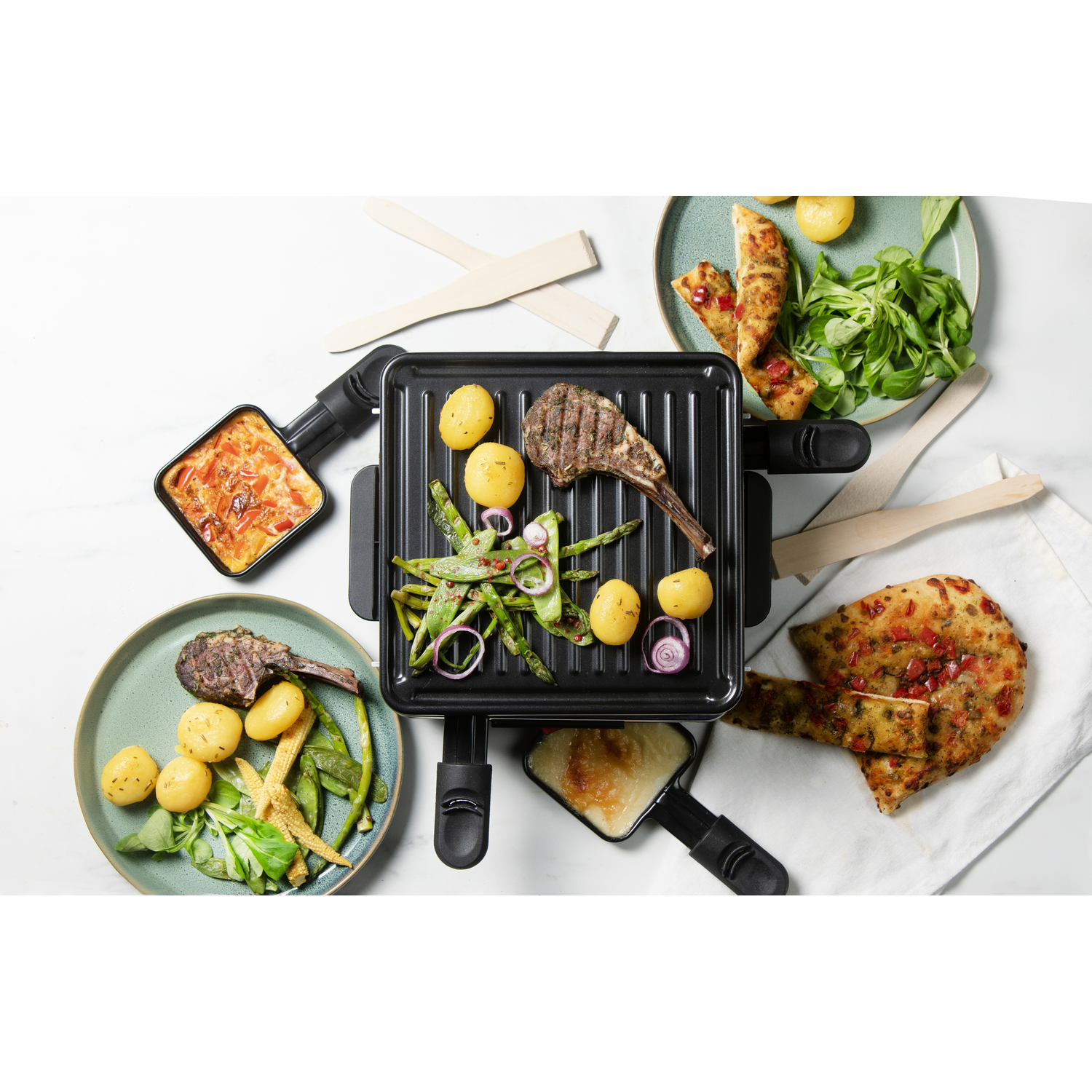 Raclette grill with cooked food and plates.