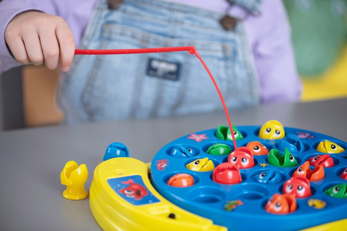 A child's hand with a red fishing rod over a toy game.