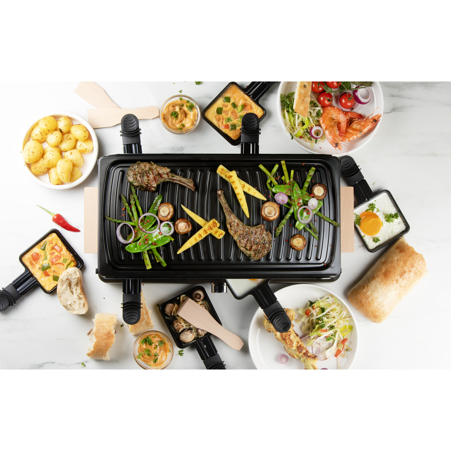 Raclette grill met diverse gegrilde gerechten op een wit oppervlak.