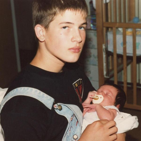 Teenager hält ein Baby. Baby in einem Strampler mit Schnuller. Schlafzimmerumgebung.