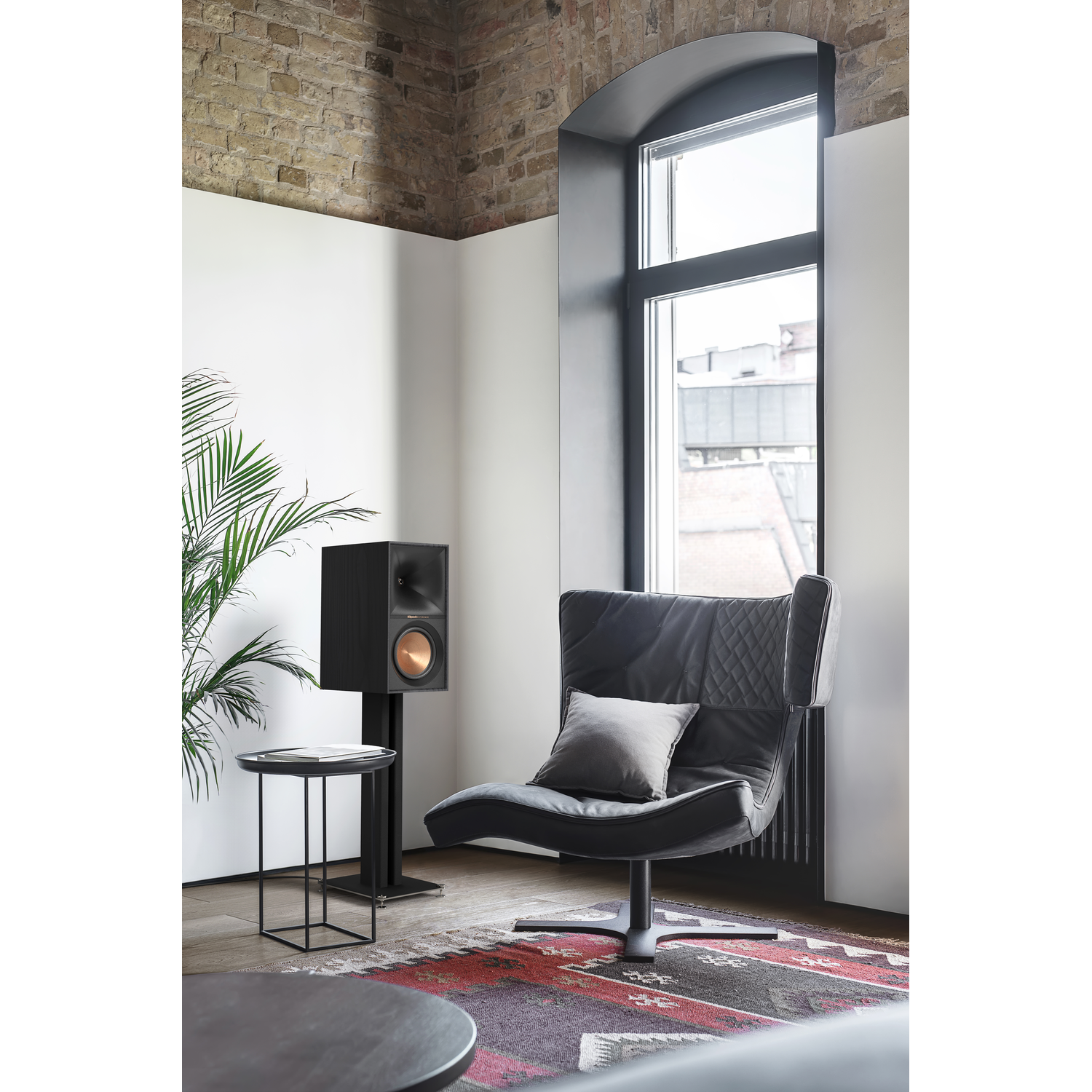 A room with a speaker on a stand, a chair, and a side table.